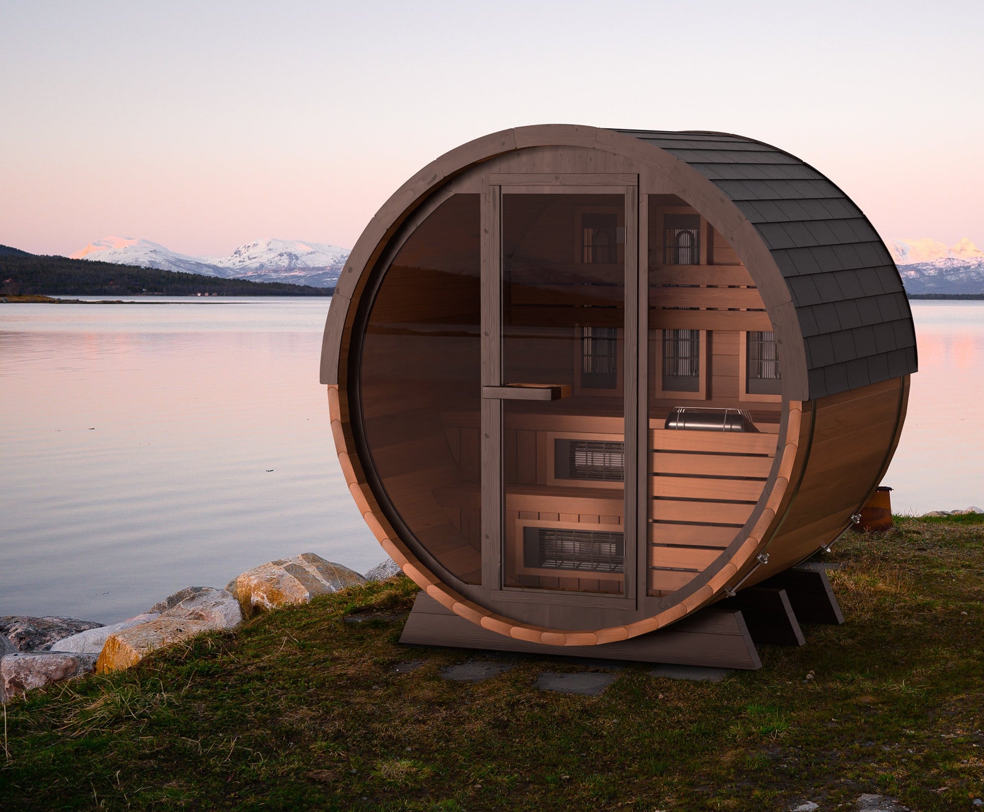 Wooden barrel-shaped sauna by a lake with mountains in the background