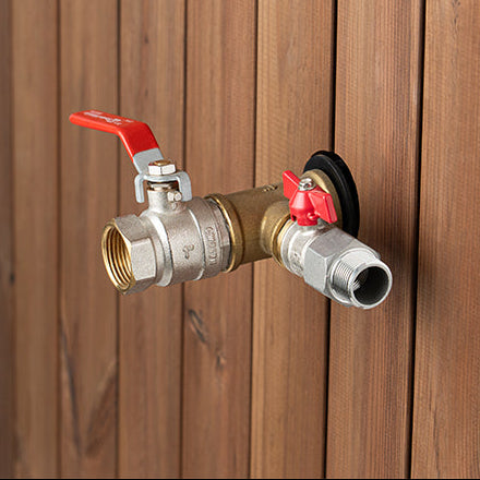 Brass outdoor faucet with red handles attached to a wooden wall.