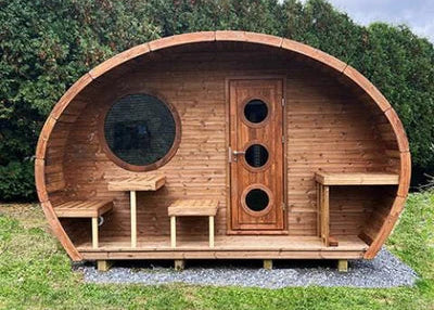 Wooden pod structure with circular windows and doors on a grassy area with trees in the background