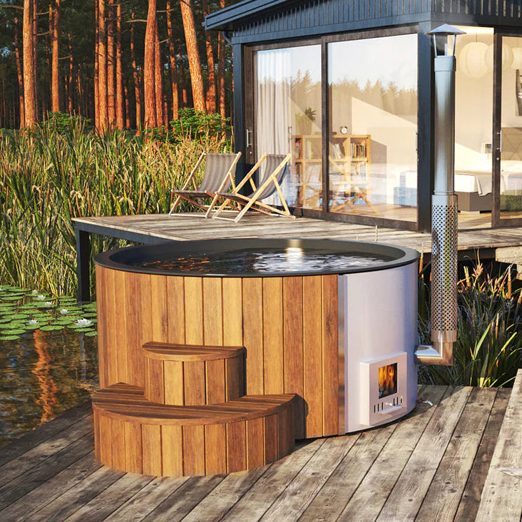 Modern cabin with a hot tub on a wooden deck by a body of water.