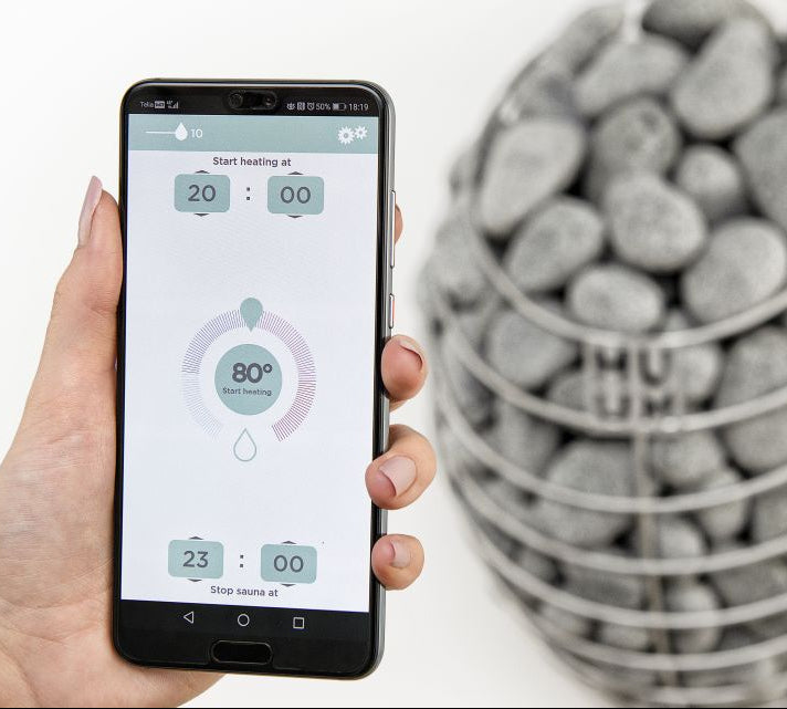Hand holding a smartphone with a temperature app displayed next to a container of stones.